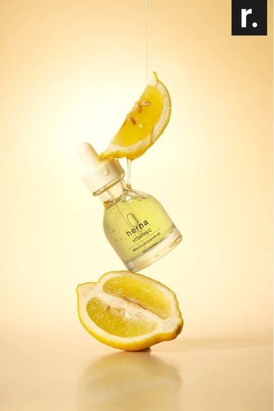 A high-quality product photography shot featuring a bottle of Vitamin C serum suspended between two lemon halves, emphasizing natural ingredients.